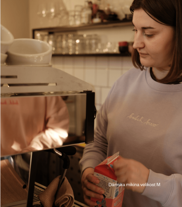 Baristka připravuje kávu v lila mikině s nápisem "batch brew"