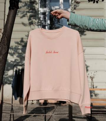 Světlá broskvová mikina s nápisem „batch brew“ z legendární kafíčkové kolekce Café Jen, vyšitá červenou nití, vyfocená venku na ramínku.